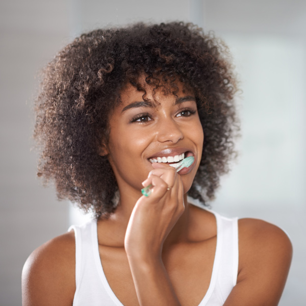 young woman brushing teeth in mirror